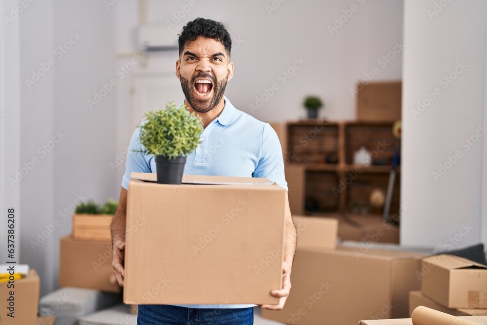 Hispanic man with beard moving to a new home holding box angry and mad screaming frustrated and furious, shouting with anger looking up. Hispanic man with beard moving to a new home holding box angry and mad screaming frustrated and furious, shouting with anger looking up.
