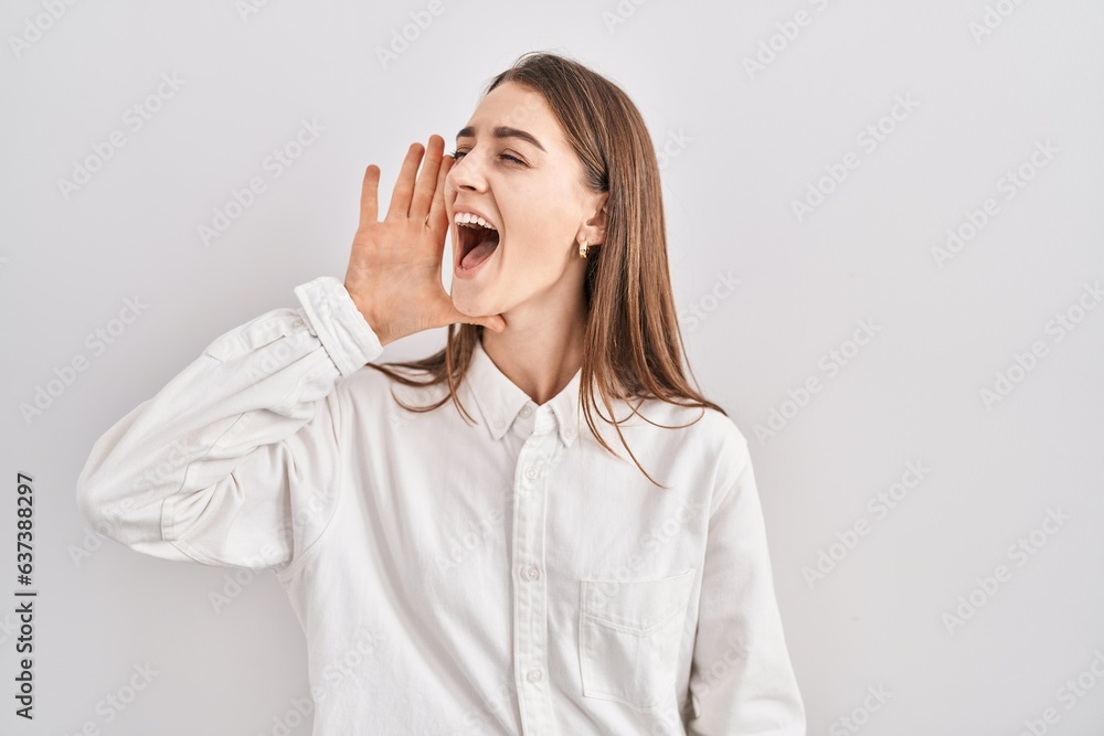 Young caucasian woman standing over isolated background shouting and screaming loud to side with hand on mouth. communication concept. Young caucasian woman standing over isolated background shouting and screaming loud to side with hand on mouth. communication concept.