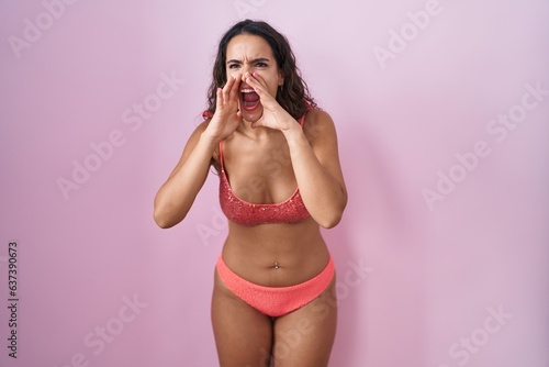 Young hispanic woman wearing lingerie over pink background shouting angry out loud with hands over mouth