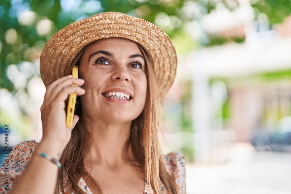 Young woman tourist wearing summer hat talking on smartphone at street