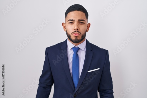 Young hispanic man wearing business suit and tie looking at the camera blowing a kiss on air being lovely and sexy. love expression.