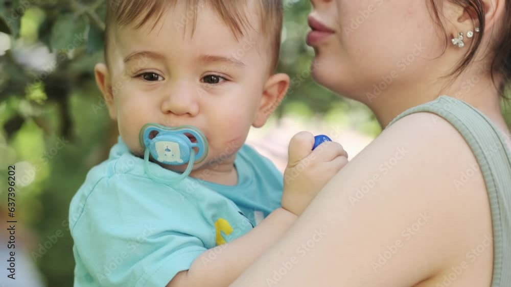 A little boy in his mother's arms is trying to pick green apples from a tree branch A little boy in his mother's arms is trying to pick green apples from a tree branch