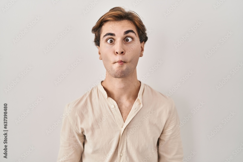Young man standing over isolated background making fish face with lips, crazy and comical gesture. funny expression. Young man standing over isolated background making fish face with lips, crazy and comical gesture. funny expression.