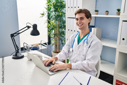Young caucasian man doctor smiling confident using laptop working at clinic