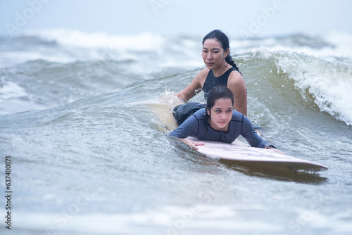 Pretty teen girl learns to surf with a female trainer nearby, extreme outdoor water sports