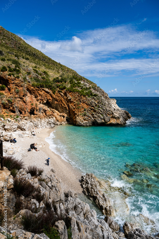 A secluded bay with white sand and turquoise waters in the Mediterranean Sea between the rocks of the Zingaro National Park in Sicily in the sun