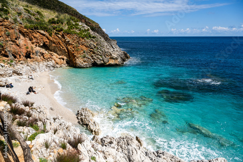 A secluded bay with white sand and turquoise waters in the Mediterranean Sea between the rocks of the Zingaro National Park in Sicily in the sun