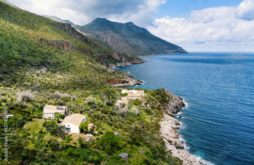 On the coast in the Zingaro National Park, between green mountains and the blue Mediterranean Sea, there are small white cottages.