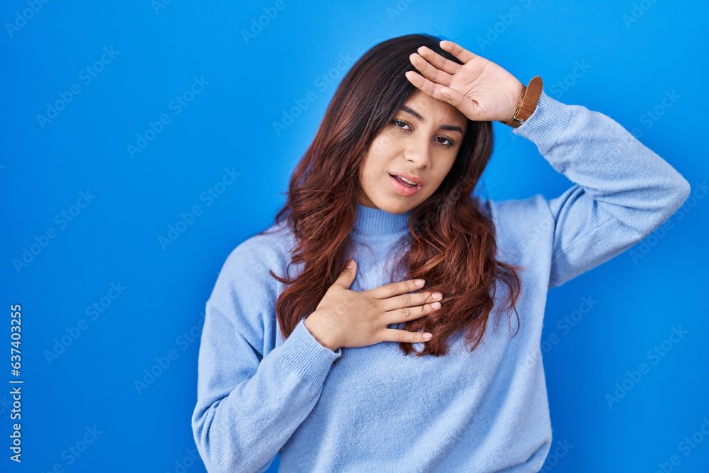 Hispanic young woman standing over blue background touching forehead for illness and fever, flu and cold, virus sick Hispanic young woman standing over blue background touching forehead for illness and fever, flu and cold, virus sick