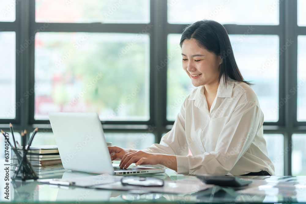 Young asian female office worker sitting in bright office and working on computer laptop.. Young asian female office worker sitting in bright office and working on computer laptop..