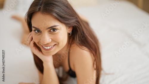 Young beautiful hispanic woman wearing lingerie lying on bed smiling at bedroom