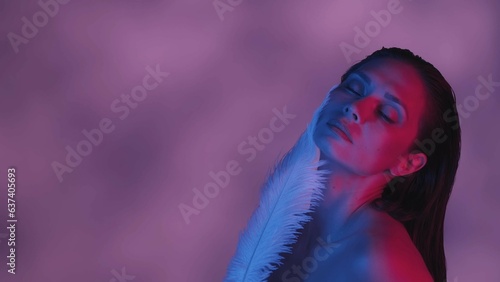 Close up shot of a seminaked young woman covering herself with two feathers in blue and pink color scheme and shadowed background. photo