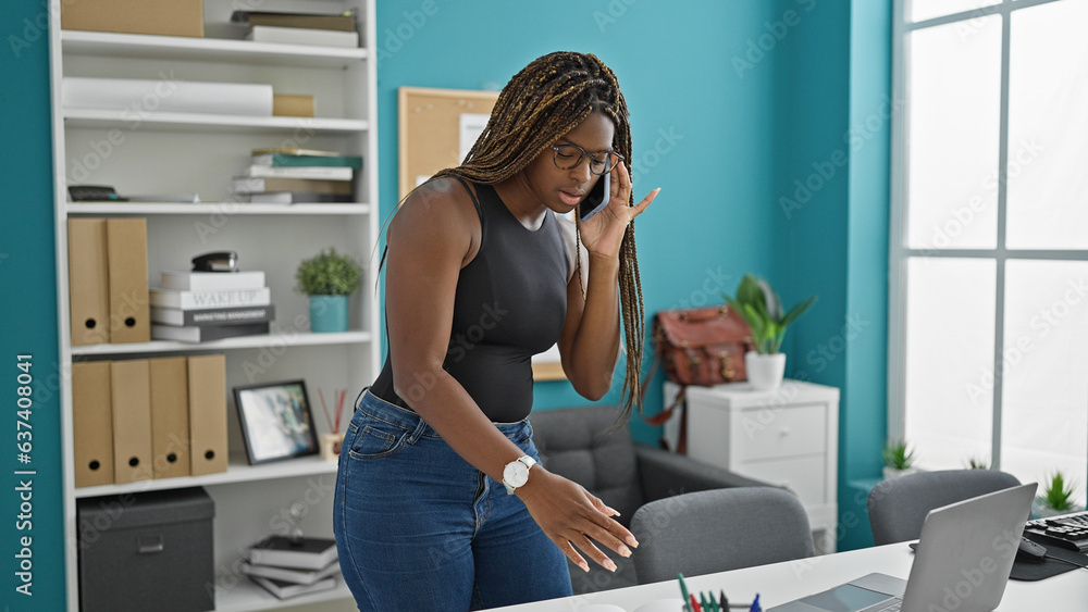 African american woman business worker using laptop talking on smartphone at the office African american woman business worker using laptop talking on smartphone at the office