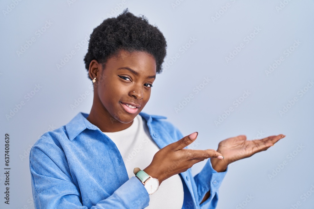 African american woman standing over blue background inviting to enter smiling natural with open hand African american woman standing over blue background inviting to enter smiling natural with open hand