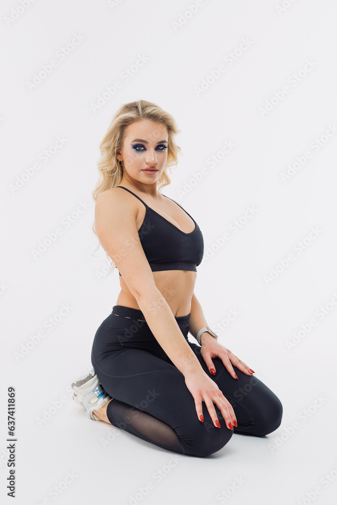 A sports model is sitting on a white floor. The model poses and looks at the camera