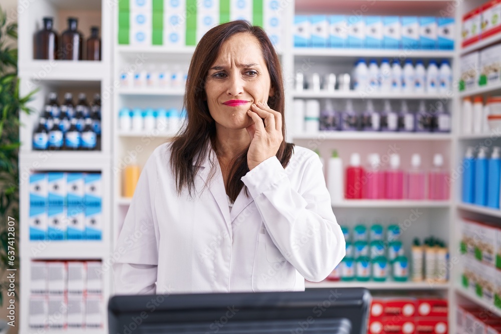 Middle age brunette woman working at pharmacy drugstore touching mouth with hand with painful expression because of toothache or dental illness on teeth. dentist