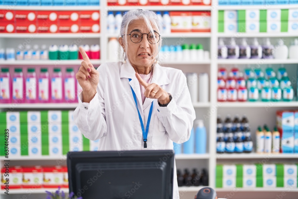 Middle age woman with tattoos working at pharmacy drugstore pointing aside worried and nervous with both hands, concerned and surprised expression Middle age woman with tattoos working at pharmacy drugstore pointing aside worried and nervous with both hands, concerned and surprised expression