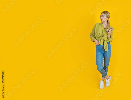 Look aside copy space, full body front view young European blonde girl look aside copy space. Holding mobile cell phone, using smartphone. Advert, banner, offer text workspace area concept image.