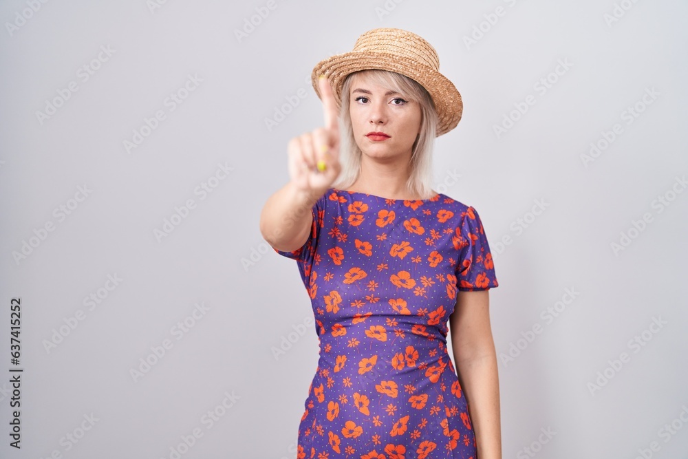 Young caucasian woman wearing flowers dress and summer hat pointing with finger up and angry expression, showing no gesture Young caucasian woman wearing flowers dress and summer hat pointing with finger up and angry expression, showing no gesture
