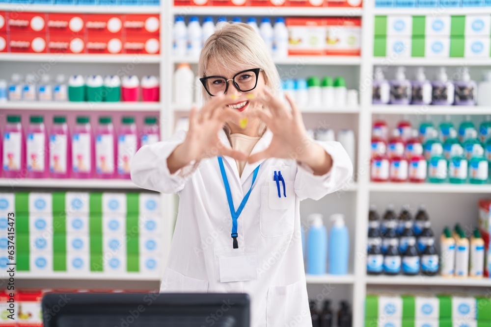 Young caucasian woman working at pharmacy drugstore smiling in love doing heart symbol shape with hands. romantic concept.