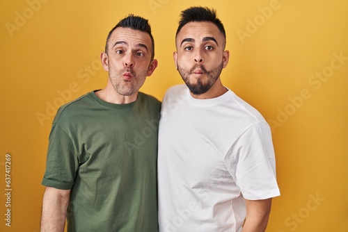 Homosexual couple standing over yellow background making fish face with lips, crazy and comical gesture. funny expression.