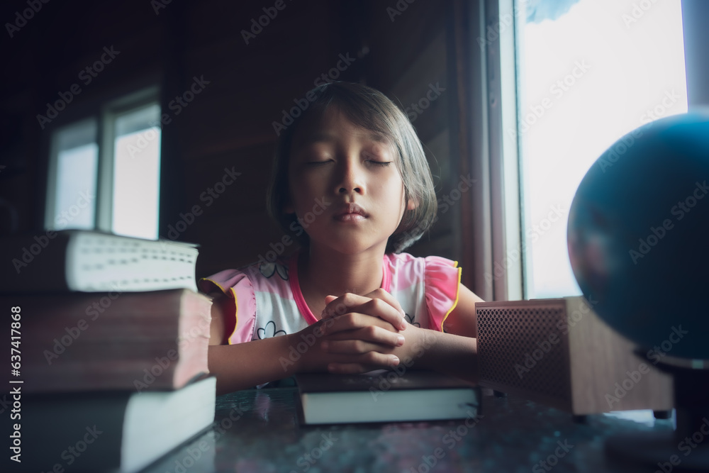 Child girl praying on bible with light in morning at home, christian concept. - obrazy, fototapety, plakaty 
