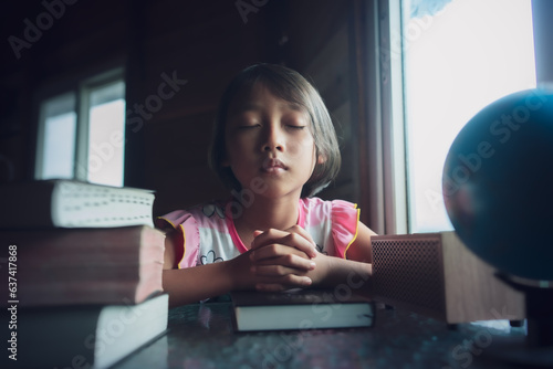 Canvastavla Child girl praying on bible with light in morning at home, christian concept