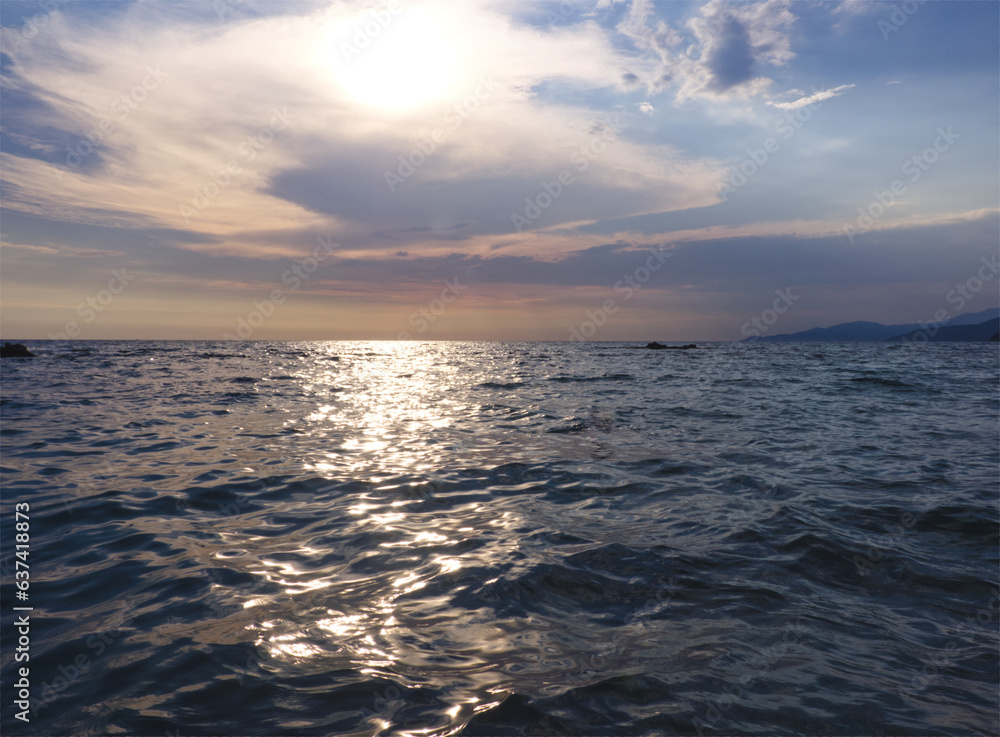Seascape water and sky background. Mediterranean Sea landscape. Sunset on Italy, Campania. Blue water surface with waves. Sunset water with sunbeams. Cloudy sky. Natural background.