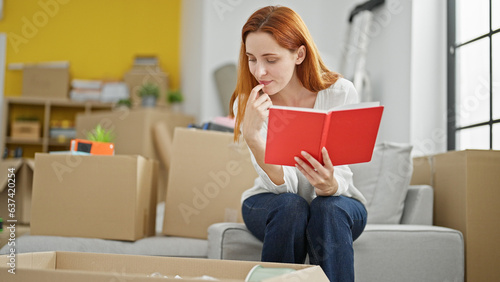 Young redhead woman unpacking cardboard box reading notebook checking at new home © Krakenimages.com