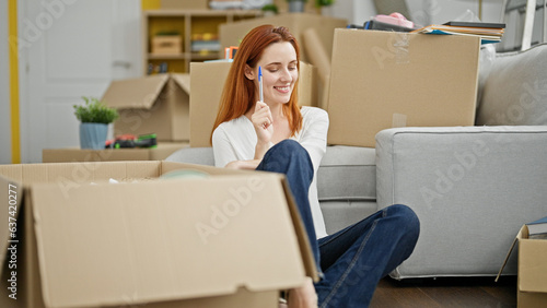 Young redhead woman sitting on floor thinking at new home