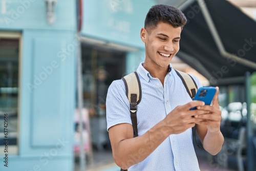 Young hispanic man student using smartphone at street