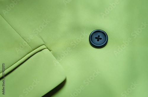 Black button is sewn on green cotton fabric closeup. Buttons for clothes features and selection