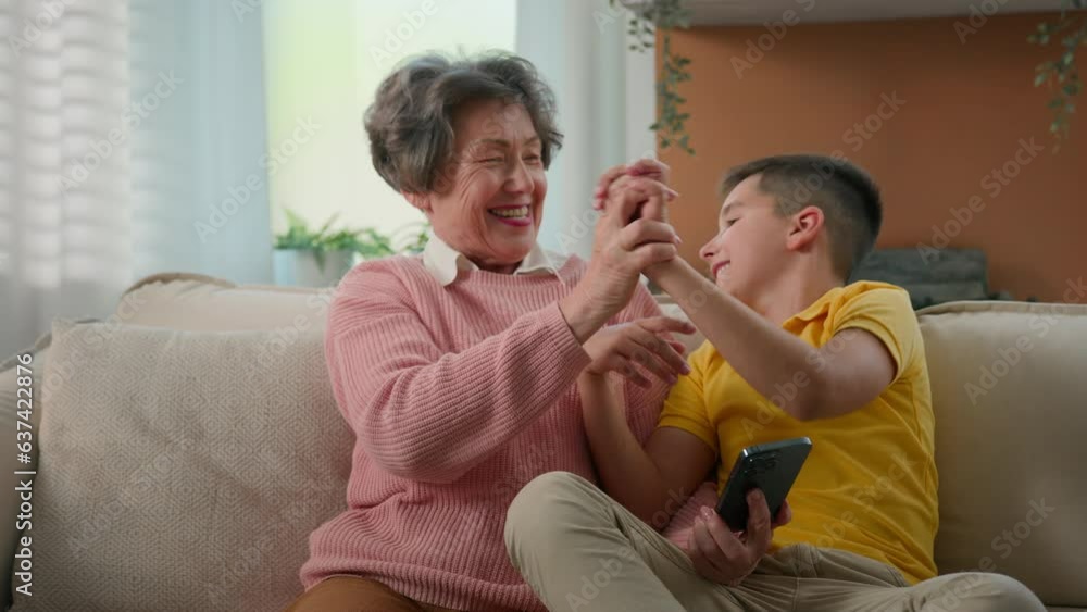 Happy funny caucasian grandmother and grandson playing mobile phone together at home couch give high five hands grandma with kid boy celebrating victory in online game on smartphone teamwork success Happy funny caucasian grandmother and grandson playing mobile phone together at home couch give high five hands grandma with kid boy celebrating victory in online game on smartphone teamwork success