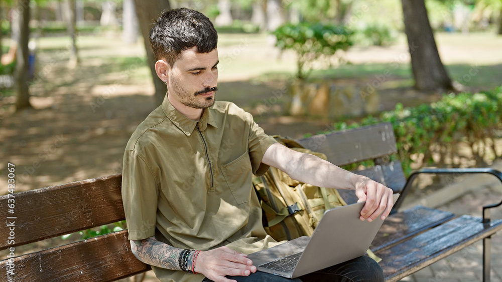 Young hispanic man tourist using laptop sitting on bench at park Young hispanic man tourist using laptop sitting on bench at park