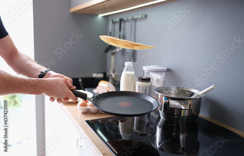 Hands hold black iron pan and toss pancake into air. Cooking pancakes at home in kitchen