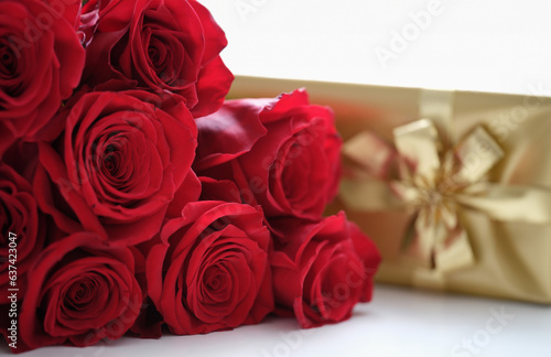 Fresh red roses and golden gift box on white table. Valentine day and surprise for woman