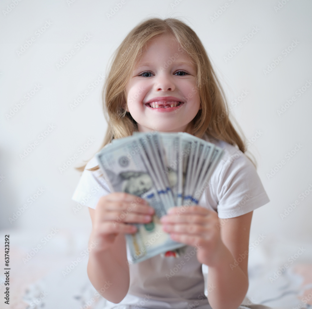 Portrait of happy smiling little girl with fan of dollars. Financial earnings in childhood concept