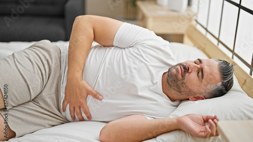 Grey-haired man suffering for stomach ache lying on bed at bedroom
