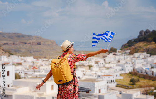 Young traveling woman with national greek flag enjoying view of Lindos. Travel to Greece, Mediterranean islands outside tourist season.