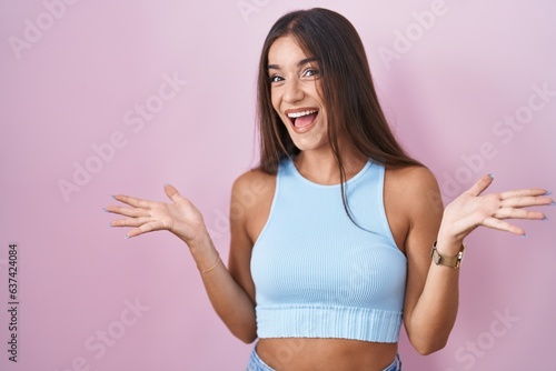 Young brunette woman standing over pink background celebrating crazy and amazed for success with arms raised and open eyes screaming excited. winner concept