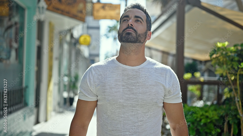Young hispanic man looking to the sky with serious expression at street Young hispanic man looking to the sky with serious expression at street