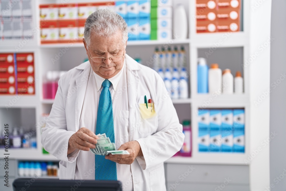 Middle age grey-haired man pharmacist counting dollars at pharmacy Middle age grey-haired man pharmacist counting dollars at pharmacy