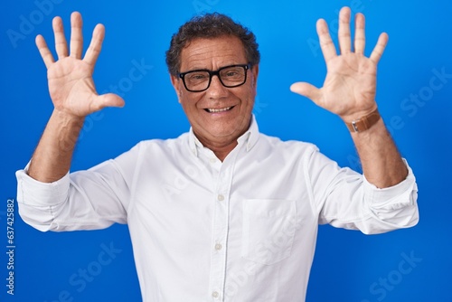 Middle age hispanic man standing over blue background showing and pointing up with fingers number ten while smiling confident and happy.