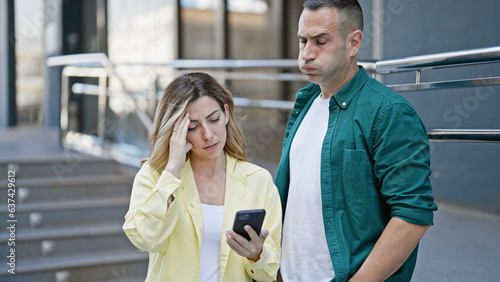 Man and woman couple using smartphone worried at street