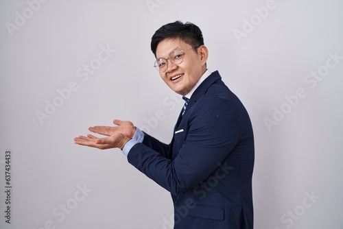 Young asian man wearing business suit and tie pointing aside with hands open palms showing copy space, presenting advertisement smiling excited happy