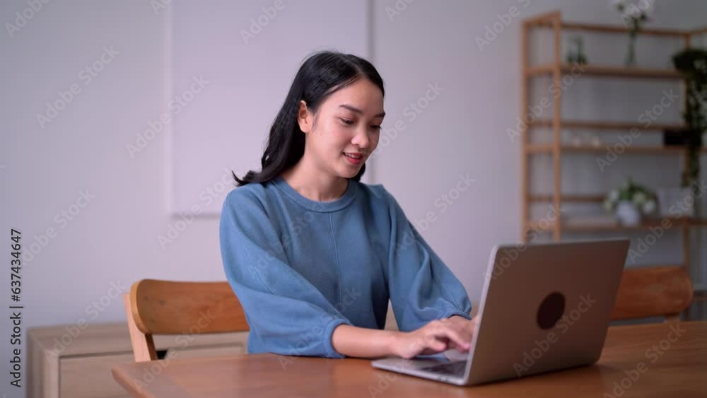 happy positive Asian woman using her laptop working on pc sitting on chair at home happy positive Asian woman using her laptop working on pc sitting on chair at home