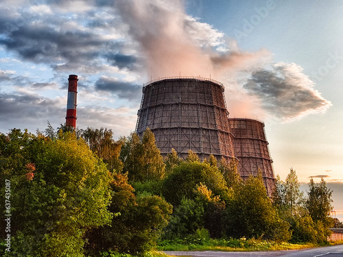 CHP cooling towers from which smoke is coming out against blue sky. A large pipe of a thermal power plant with smoke and steam on a blue sky background photo