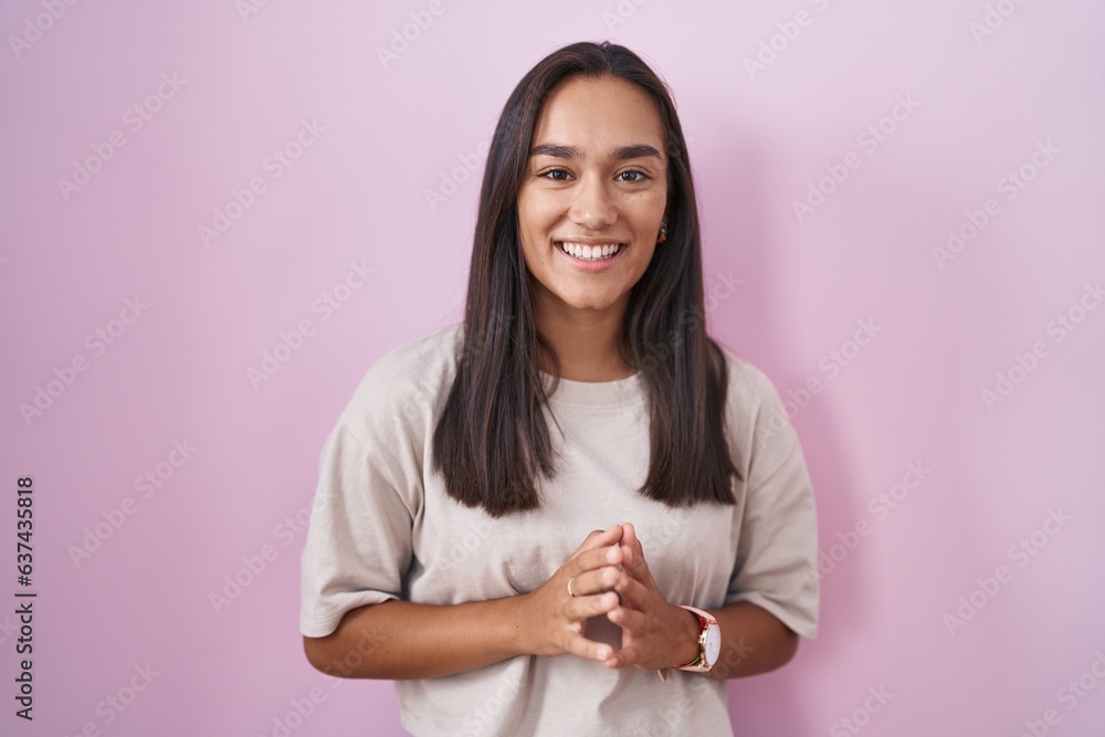Young hispanic woman standing over pink background hands together and fingers crossed smiling relaxed and cheerful. success and optimistic Young hispanic woman standing over pink background hands together and fingers crossed smiling relaxed and cheerful. success and optimistic