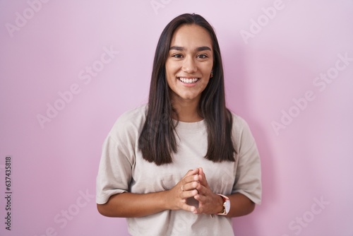 Young hispanic woman standing over pink background hands together and fingers crossed smiling relaxed and cheerful. success and optimistic