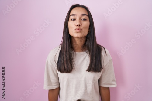 Young hispanic woman standing over pink background looking at the camera blowing a kiss on air being lovely and sexy. love expression.